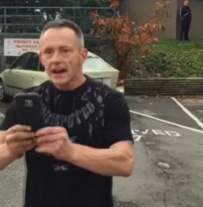 A man in a racially offensive parking lot argument in Abbotsford walks towards the camera with a cell phone.